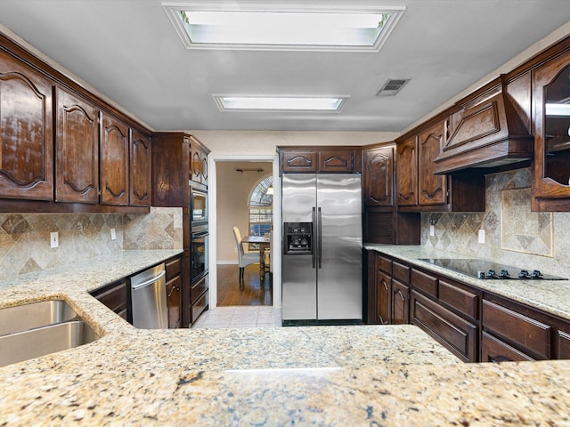 kitchen with light stone countertops, dark brown cabinets, custom range hood, and black appliances