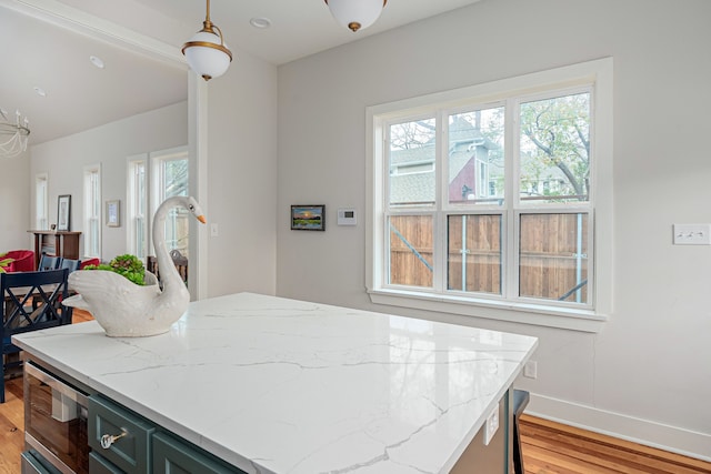 kitchen featuring decorative light fixtures, stainless steel microwave, light stone countertops, and light hardwood / wood-style flooring