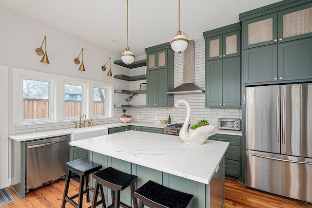 kitchen featuring light stone countertops, stainless steel appliances, wall chimney range hood, a center island, and hanging light fixtures