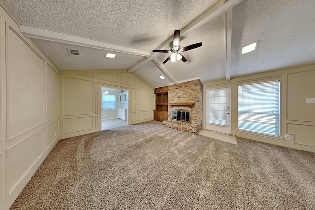 unfurnished living room featuring ceiling fan, a fireplace, lofted ceiling with beams, a textured ceiling, and light colored carpet