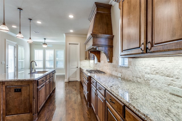 kitchen featuring light stone countertops, custom exhaust hood, a kitchen island with sink, sink, and decorative light fixtures