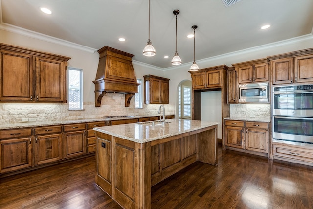 kitchen with a kitchen island with sink, hanging light fixtures, sink, crown molding, and stainless steel appliances