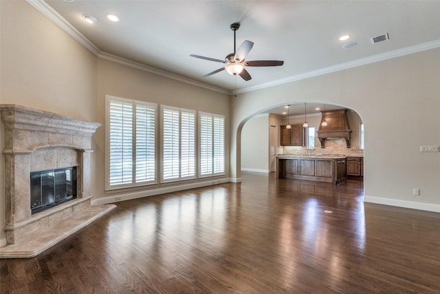 unfurnished living room with a tile fireplace, crown molding, ceiling fan, and dark hardwood / wood-style floors