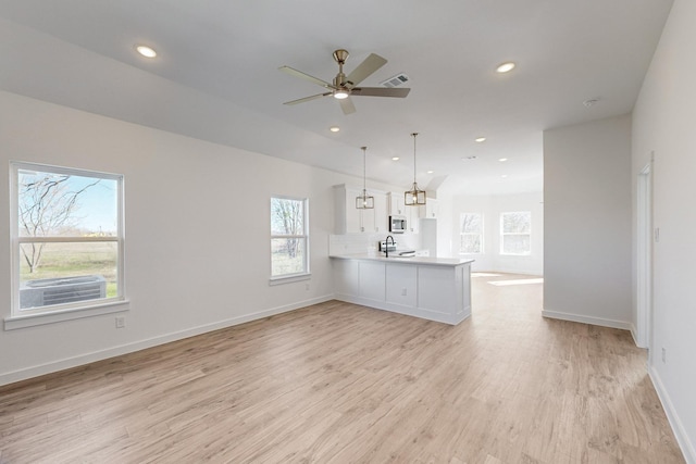 unfurnished living room featuring ceiling fan, plenty of natural light, sink, and light wood-type flooring