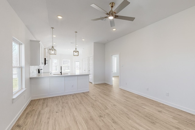 interior space with sink, kitchen peninsula, pendant lighting, light hardwood / wood-style floors, and white cabinets