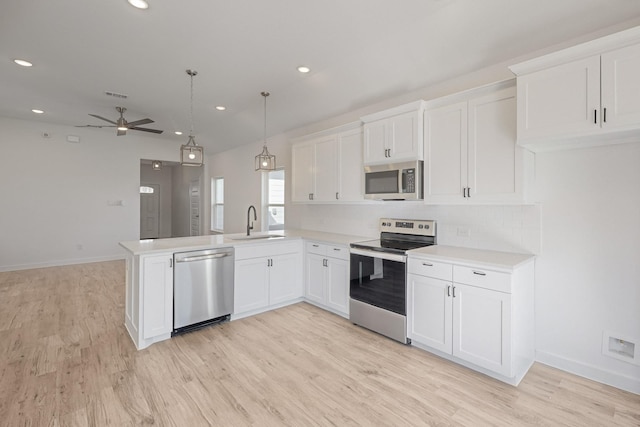 kitchen featuring kitchen peninsula, stainless steel appliances, sink, pendant lighting, and white cabinetry