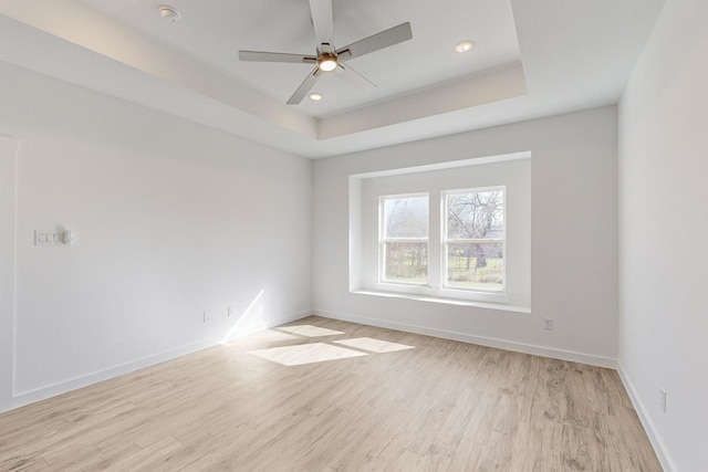 unfurnished room with ceiling fan, light hardwood / wood-style floors, and a tray ceiling