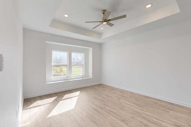 spare room with a raised ceiling, ceiling fan, and light hardwood / wood-style floors