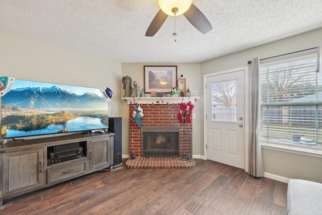 living room with a textured ceiling, dark hardwood / wood-style floors, a brick fireplace, and ceiling fan