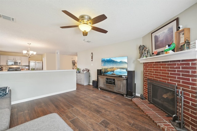 living room featuring a textured ceiling, ceiling fan with notable chandelier, a brick fireplace, and dark hardwood / wood-style flooring