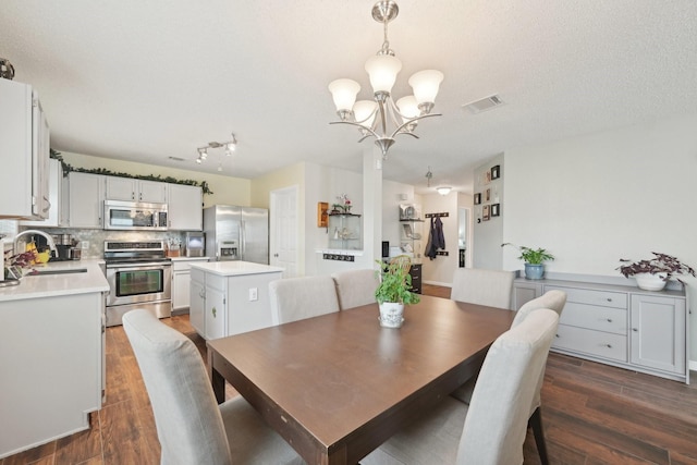 dining area featuring sink, dark wood-type flooring, a textured ceiling, and an inviting chandelier