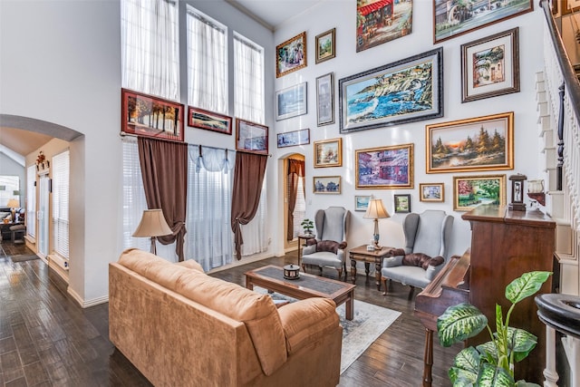 living area featuring arched walkways, baseboards, dark wood finished floors, and a high ceiling