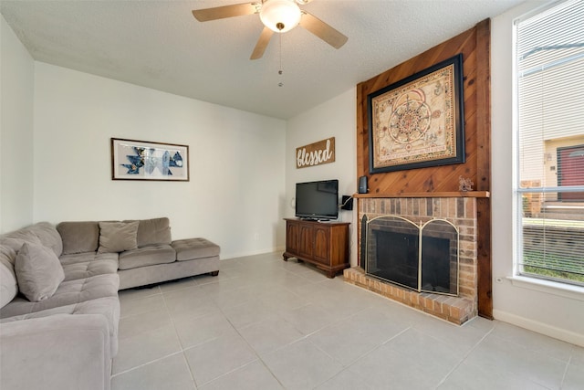 tiled living room featuring a brick fireplace, a textured ceiling, and ceiling fan