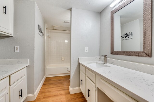 full bathroom with tiled shower / bath, vanity, wood-type flooring, and toilet