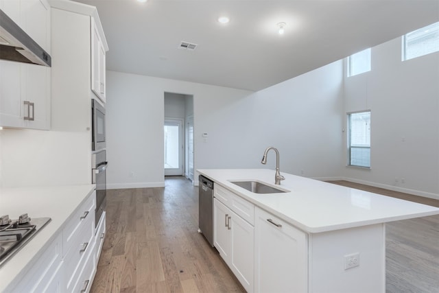 kitchen with sink, light wood-type flooring, appliances with stainless steel finishes, an island with sink, and white cabinets