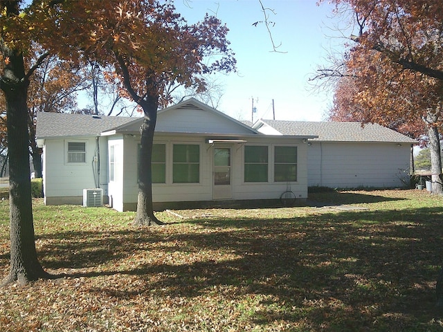 rear view of property with central air condition unit and a lawn