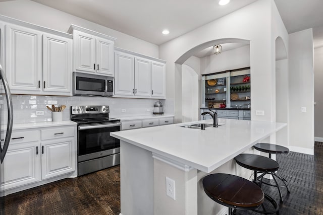 kitchen with appliances with stainless steel finishes, white cabinetry, sink, a kitchen breakfast bar, and a kitchen island with sink