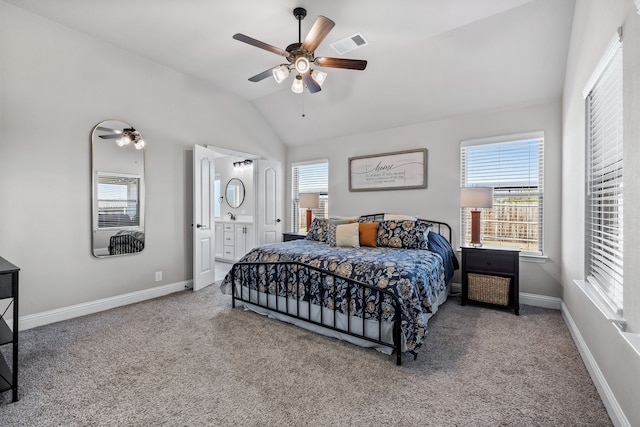 carpeted bedroom with ceiling fan, ensuite bathroom, vaulted ceiling, and multiple windows