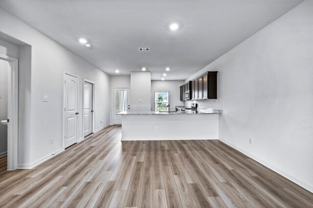 kitchen featuring kitchen peninsula, appliances with stainless steel finishes, light wood-type flooring, dark brown cabinetry, and sink