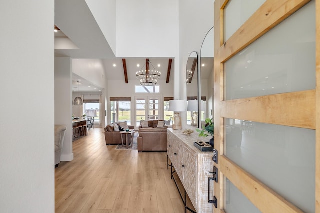 living room with beamed ceiling, light hardwood / wood-style floors, a high ceiling, and an inviting chandelier