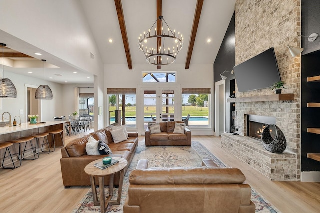 living room featuring beam ceiling, light hardwood / wood-style flooring, high vaulted ceiling, a fireplace, and a chandelier