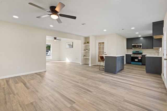 kitchen with appliances with stainless steel finishes, a kitchen island, a kitchen bar, light hardwood / wood-style floors, and ceiling fan