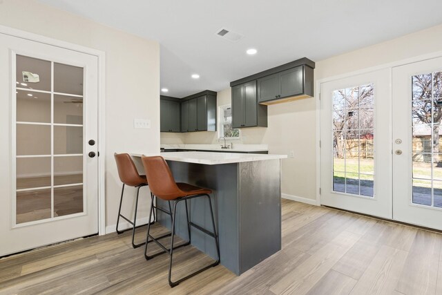 kitchen with kitchen peninsula, a breakfast bar area, light wood-type flooring, french doors, and sink