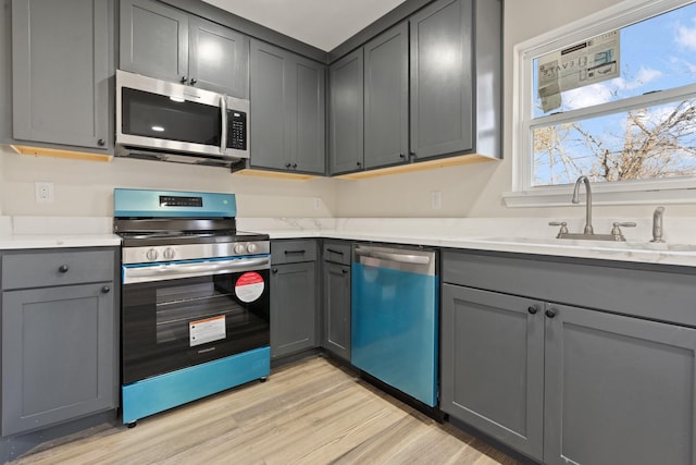 kitchen featuring light stone countertops, appliances with stainless steel finishes, light hardwood / wood-style floors, sink, and gray cabinetry