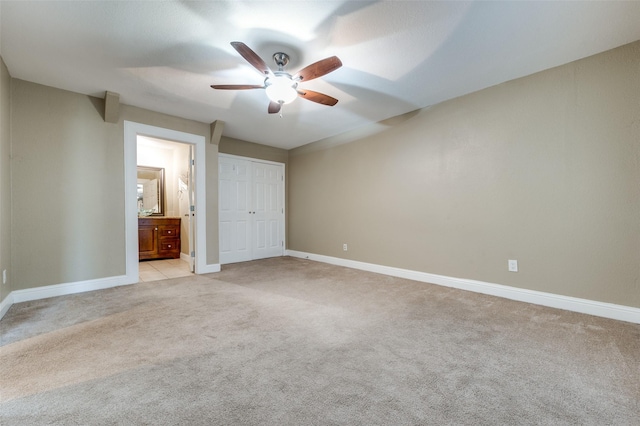 unfurnished bedroom featuring ceiling fan, light colored carpet, ensuite bath, and a closet