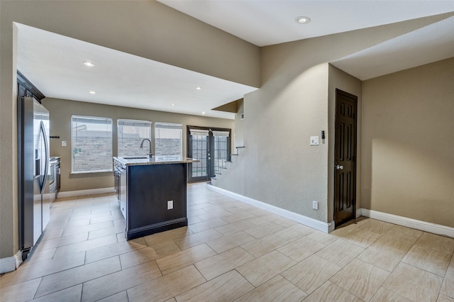 kitchen with stainless steel fridge with ice dispenser, sink, light stone counters, and a center island with sink