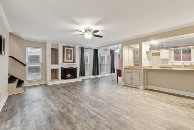 unfurnished living room with ceiling fan, light hardwood / wood-style floors, ornamental molding, and a brick fireplace