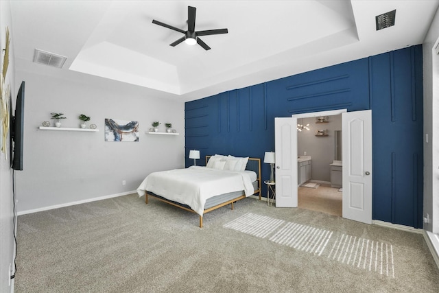 bedroom with ceiling fan with notable chandelier, carpet floors, a raised ceiling, and ensuite bathroom