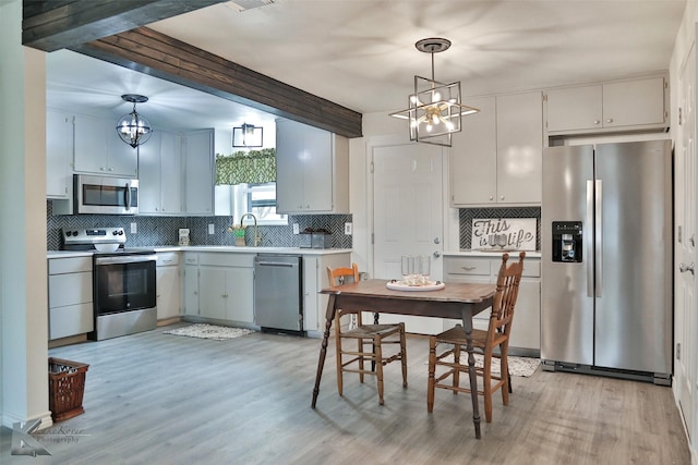 kitchen with appliances with stainless steel finishes, light wood-type flooring, backsplash, sink, and hanging light fixtures