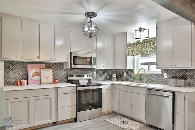 kitchen with backsplash, sink, hanging light fixtures, light hardwood / wood-style flooring, and appliances with stainless steel finishes