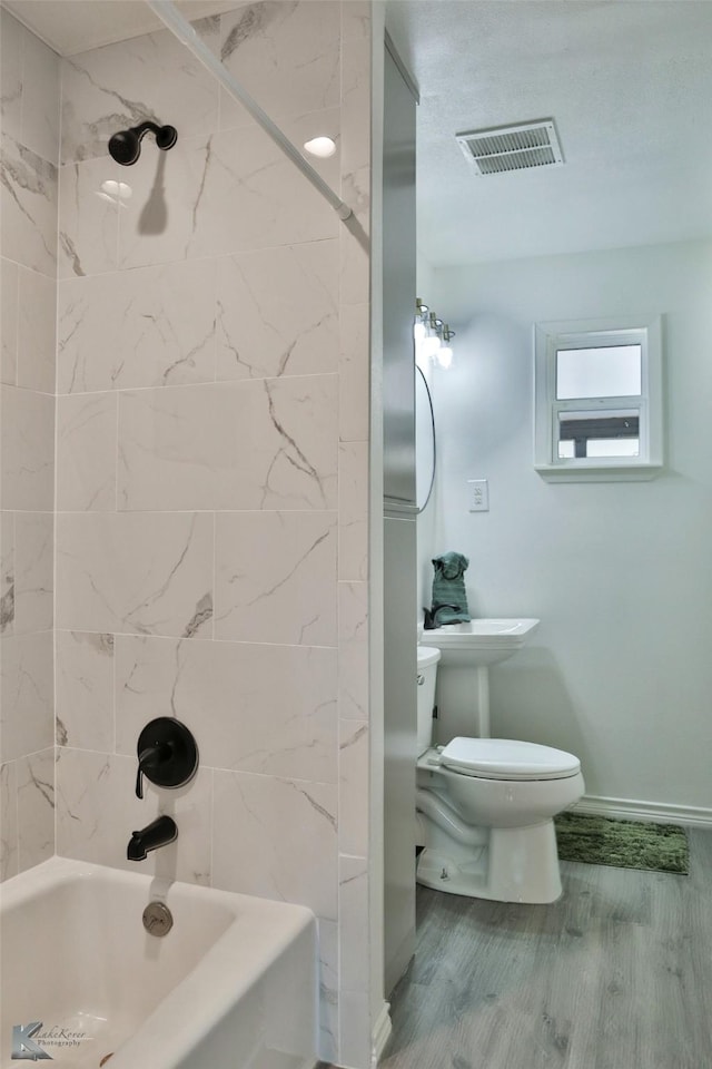 bathroom featuring wood-type flooring, tiled shower / bath combo, and toilet