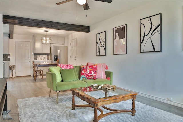 living room featuring ceiling fan with notable chandelier, beam ceiling, and light hardwood / wood-style flooring