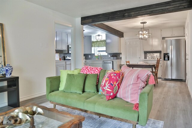 living room featuring beamed ceiling, a notable chandelier, light wood-type flooring, and sink