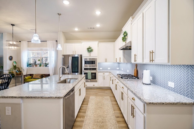 kitchen featuring pendant lighting, backsplash, a center island with sink, and stainless steel appliances