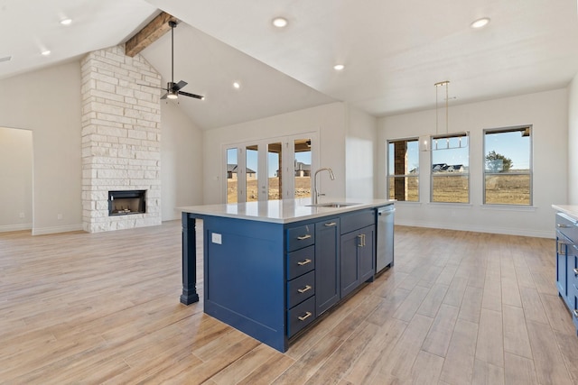 kitchen featuring stainless steel dishwasher, hanging light fixtures, sink, a stone fireplace, and a kitchen island with sink