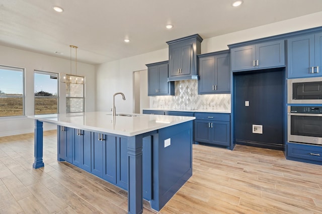 kitchen featuring built in microwave, sink, oven, hanging light fixtures, and a center island with sink