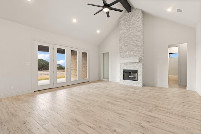 unfurnished living room with beamed ceiling, light hardwood / wood-style floors, high vaulted ceiling, and a stone fireplace