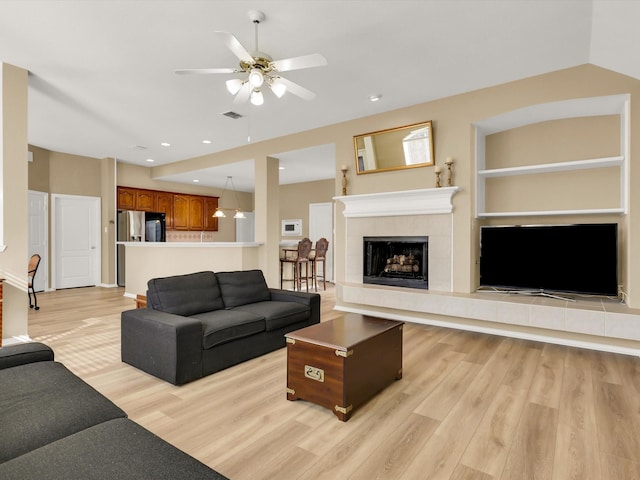 living room with a tile fireplace, ceiling fan, and light wood-type flooring