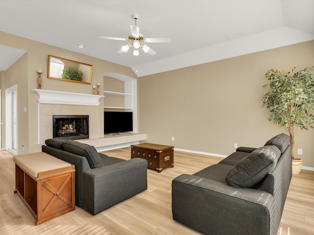 living room with lofted ceiling, light hardwood / wood-style flooring, built in features, a tile fireplace, and ceiling fan