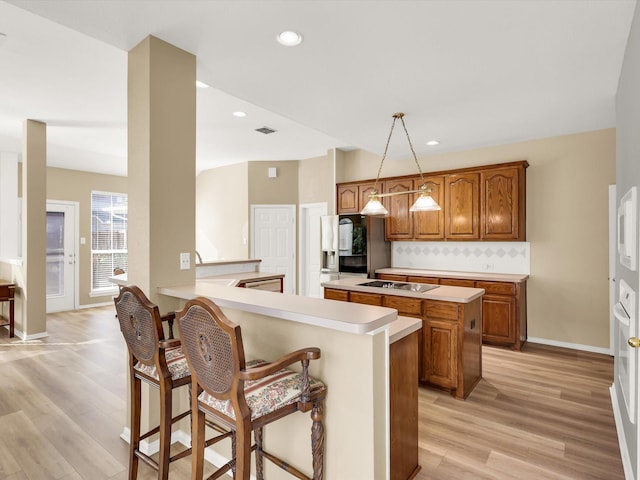 kitchen featuring pendant lighting, light hardwood / wood-style flooring, decorative backsplash, black electric cooktop, and kitchen peninsula