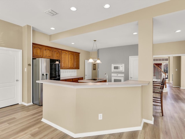 kitchen with hanging light fixtures, kitchen peninsula, white appliances, decorative backsplash, and a breakfast bar