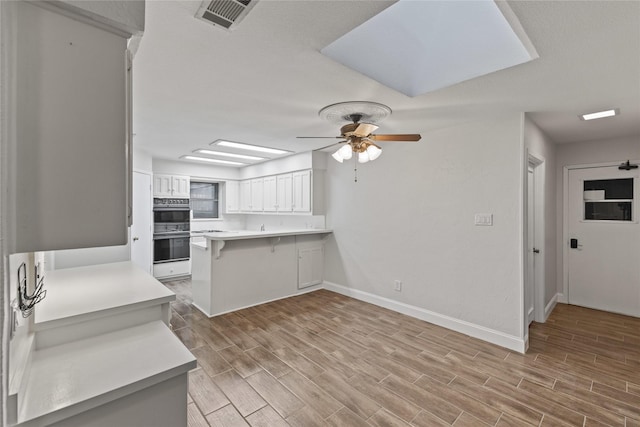 kitchen with white cabinetry, ceiling fan, kitchen peninsula, black double oven, and a breakfast bar area