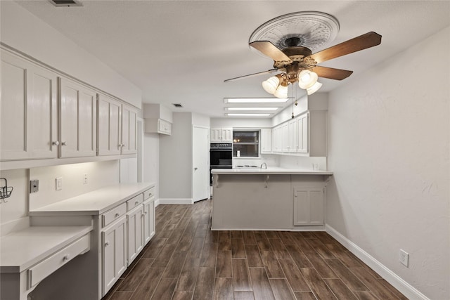 kitchen featuring white cabinetry, ceiling fan, double oven, kitchen peninsula, and a breakfast bar