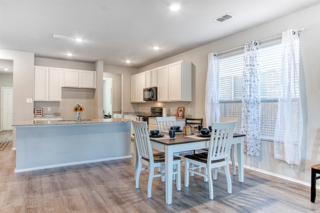 kitchen with white cabinets, light stone countertops, light hardwood / wood-style flooring, and black appliances