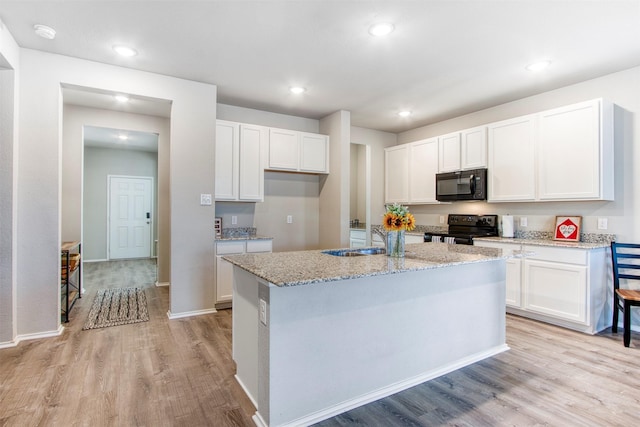 kitchen with an island with sink, sink, white cabinets, black appliances, and light stone countertops