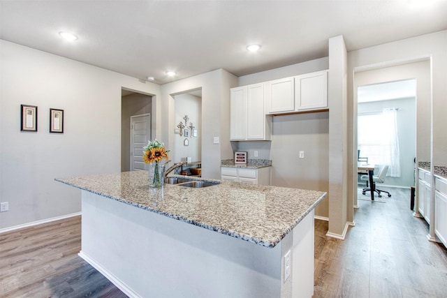 kitchen featuring a kitchen island with sink, light stone counters, and white cabinetry